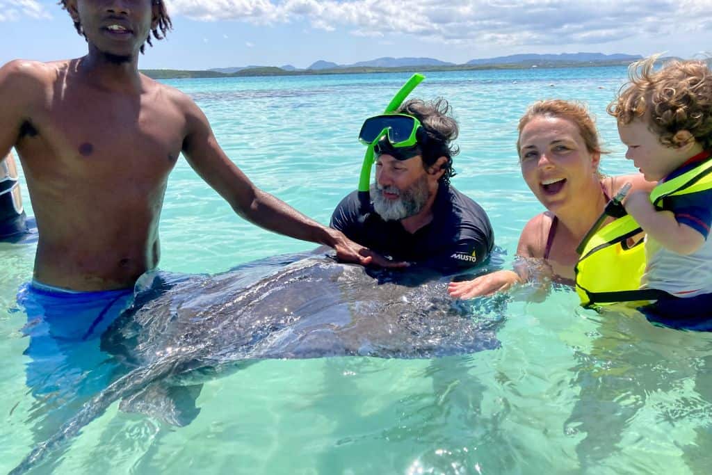 A couple are holding a stingray in the water in antigua with kids