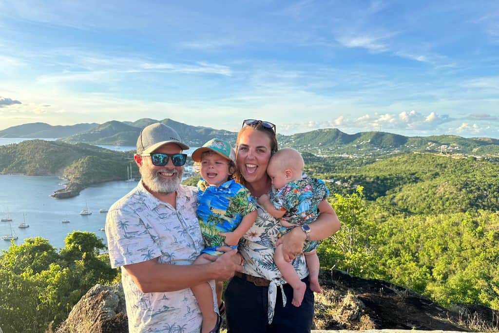 A mum, dad, toddler, and baby are all stood at the top of Shirley Heights ready for party night which is one of the best things to do in Antigua in the evening.  They are wearing Hawaiian shirts and are looking really happy.