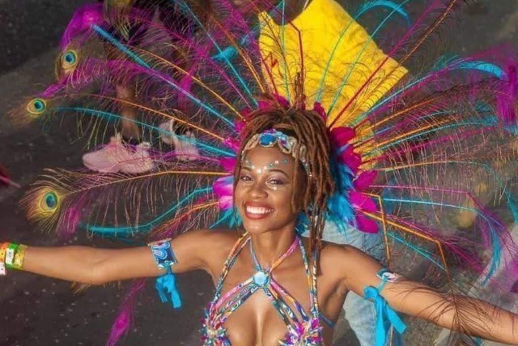 A lady in a parade outfit with pink and purple feathers at Antigua Carnival