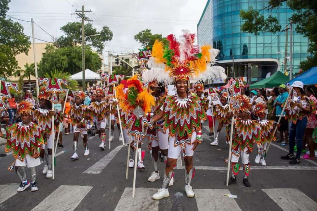 Adults and kids wearing full on parade costumes with orange, green and white feathers for Antigua Carnival
