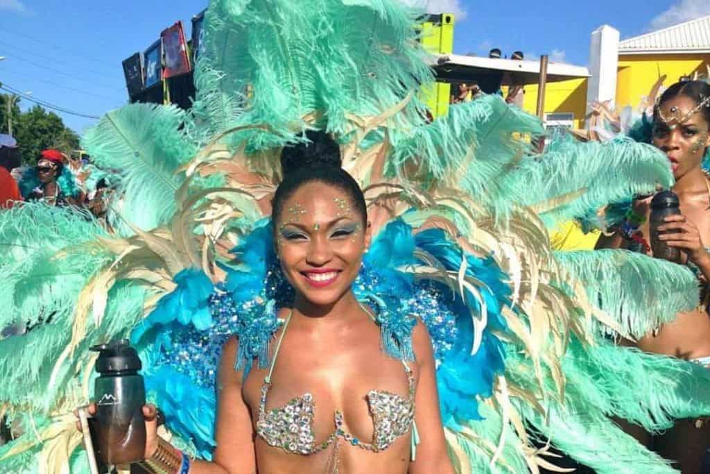 A woman in a full carnival costume with blue and green feathers at Antigua Carnival