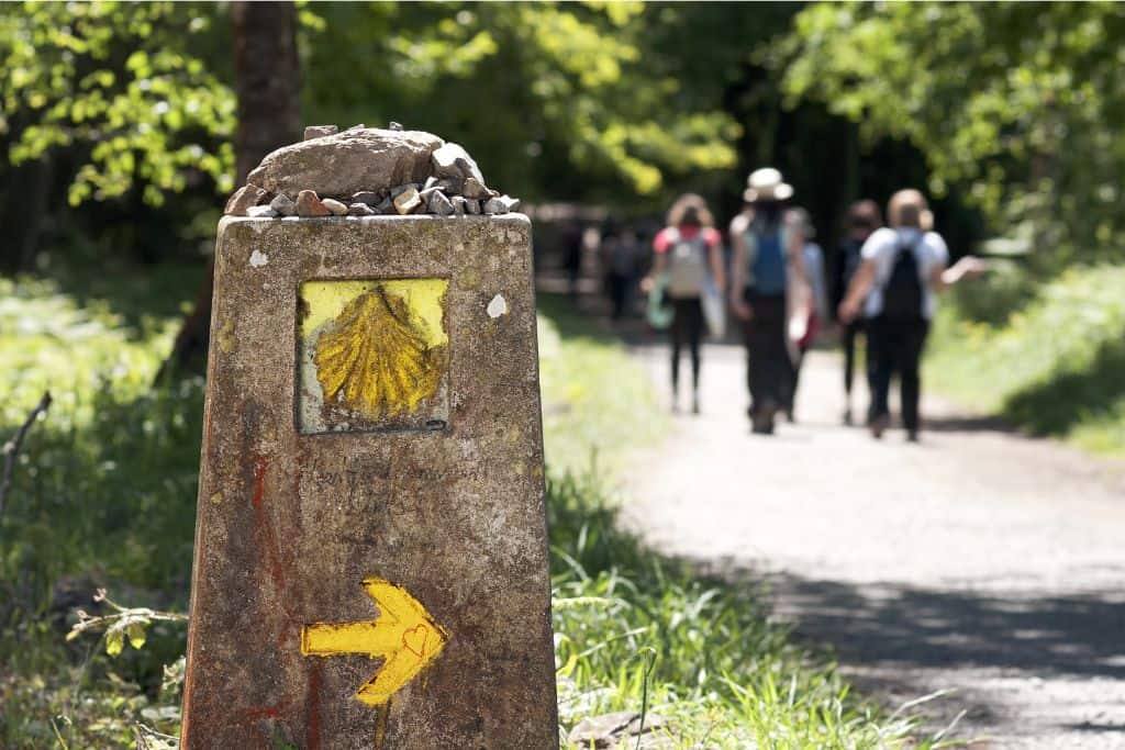 A single stone path market with a yellow arrow pointing right.  Above this is a carved out yellow seashell like a clam.  This is the sign of the Camino de Santiago which is on a lot of peoples bucket list when they visit Portugal.