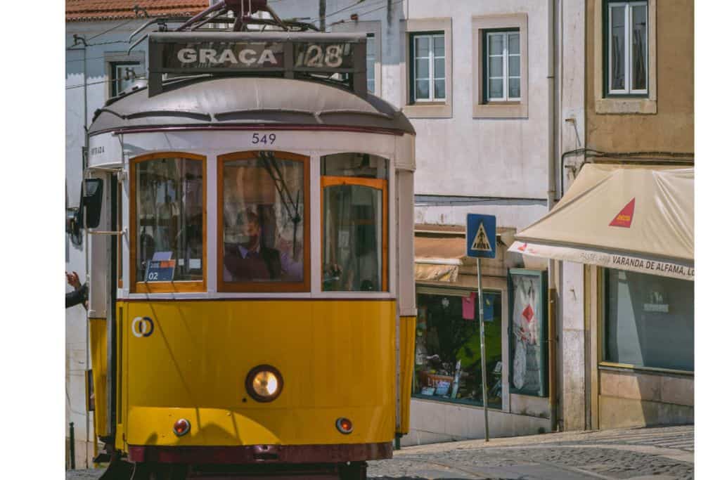 A yellow tram driving through the Graca district in Lisbon which is the best area to stay in Lisbon for a local experience.