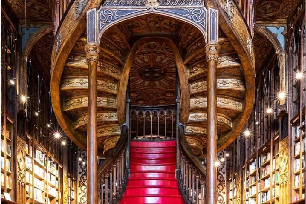 The ornate inside of the Livaria Lello Bookshop in Porto.  In the centre is the red stair case rising up and on either side are rows of books on bookshelves.