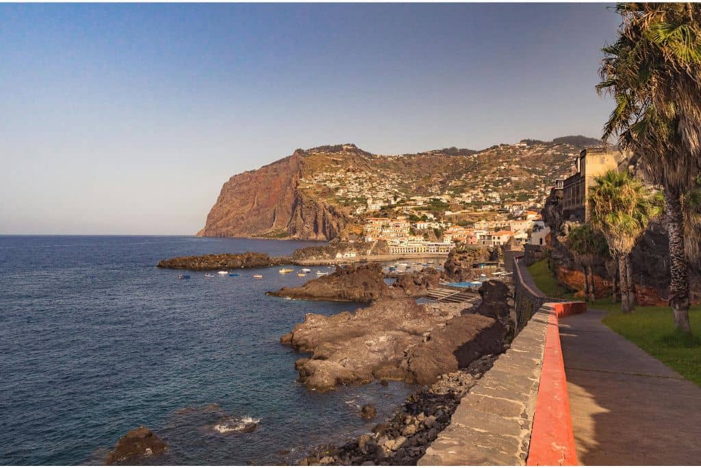 An image of a waterfront town with it's white buildings a beautiful pink colour as the sun is rising above the town in Madeira.