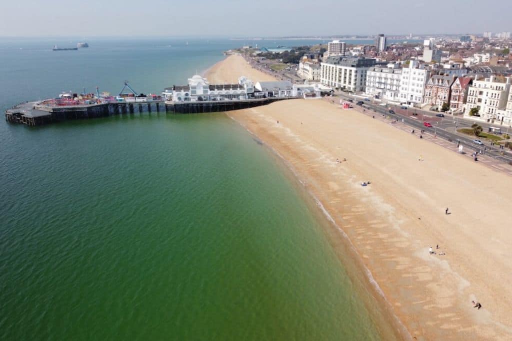 An ariel view of the pier on Southsea Beach with the white building on it and amusements.  Plus along the beach are some other buildings too.