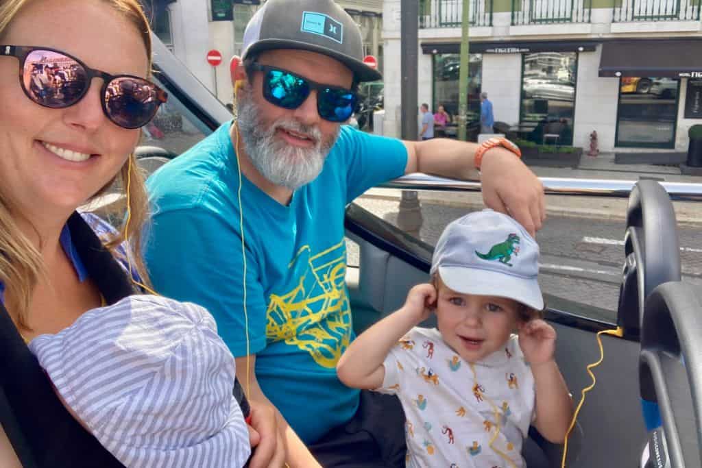 Mum, dad, baby and toddler all sat on an open topped tour bus in Lisbon.