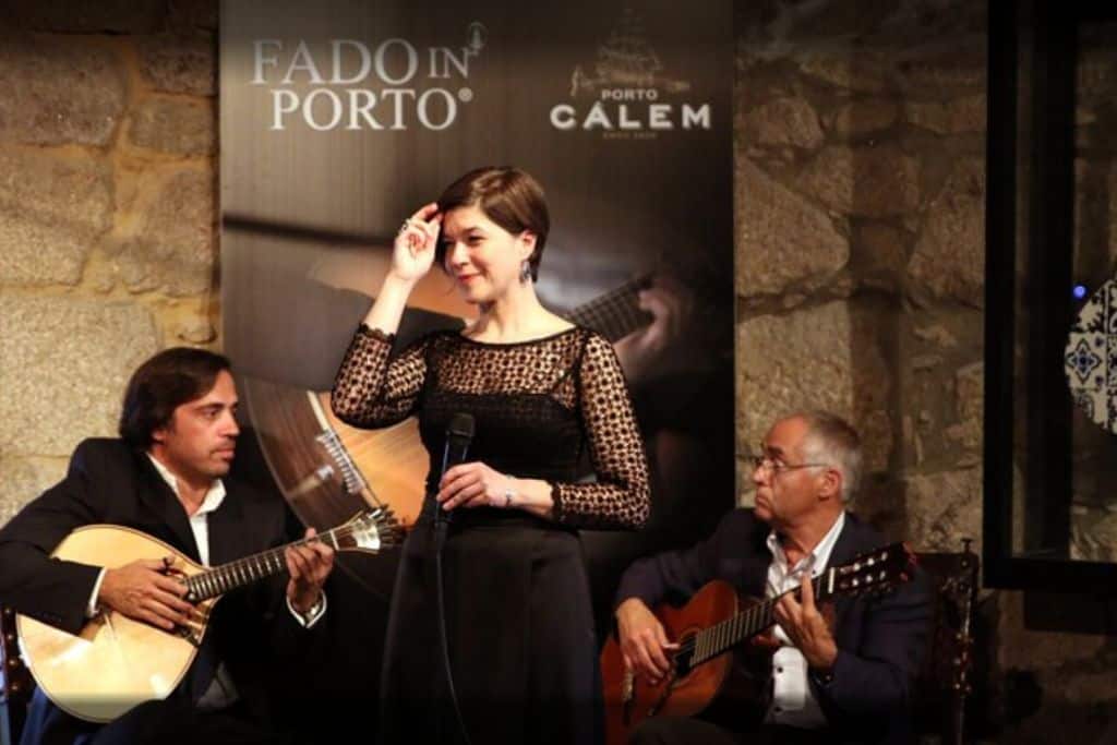 A woman and two men in singing and playing music at a Fado concert in the Calen Caves, one of the best wineries in Porto Portugal