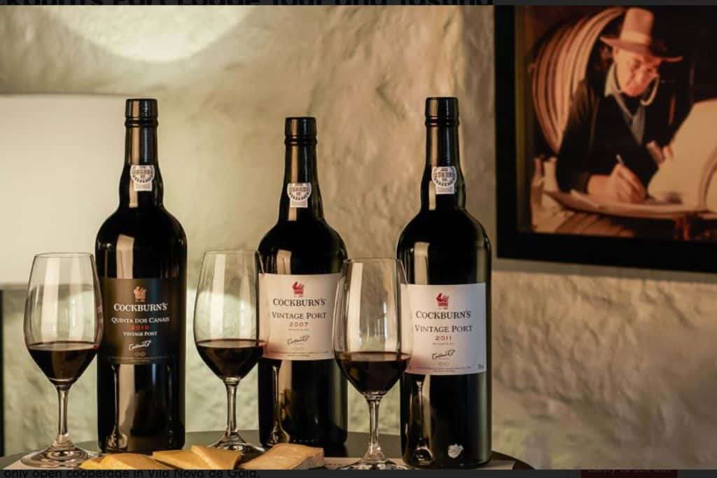 Three open bottles of port wine on bar with a one third full glass of port stood in front of each bottle as though they are prepared for a wine tasting.  Most people who visit Portugal put tasting on their bucket list.