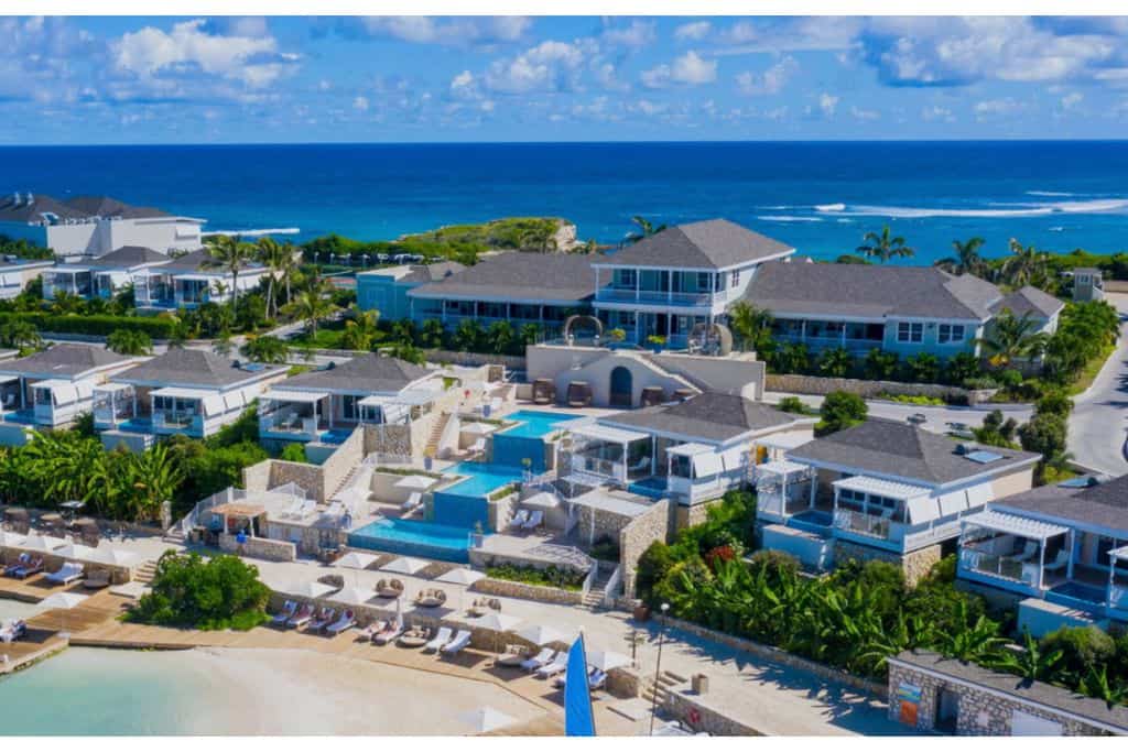 The view from the water of Hammock Cove Resorts.  There are several resort buildings such as villas and restaurants on the hillside.  In the middle is. 3 tiered infinity pool, this is the only one of the Antigua all inclusive luxury resorts to have a pool like this.