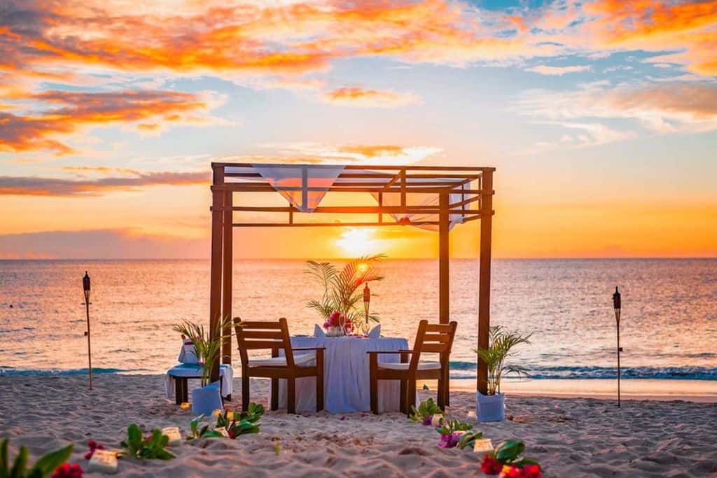 A private dining experience on the beach at the Keyonna Resort with a gzebo about the table. In the background the sun is about to set over the sea. 