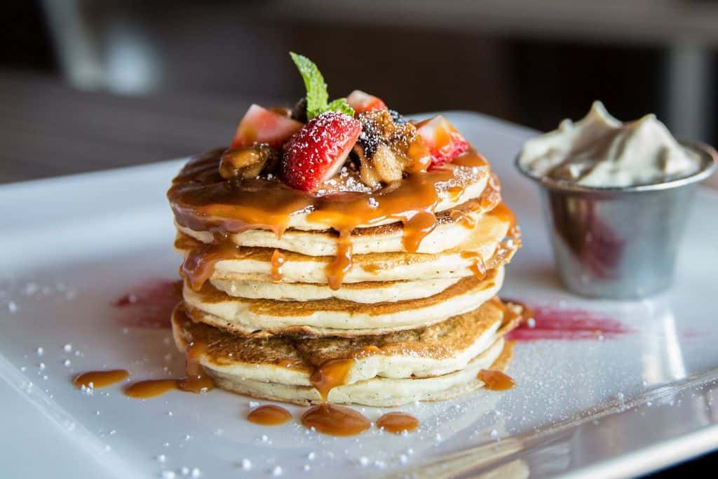 A stack of pancakes with some caramel sauce dripping down the sides. On the top are some fresh sliced fruits.
