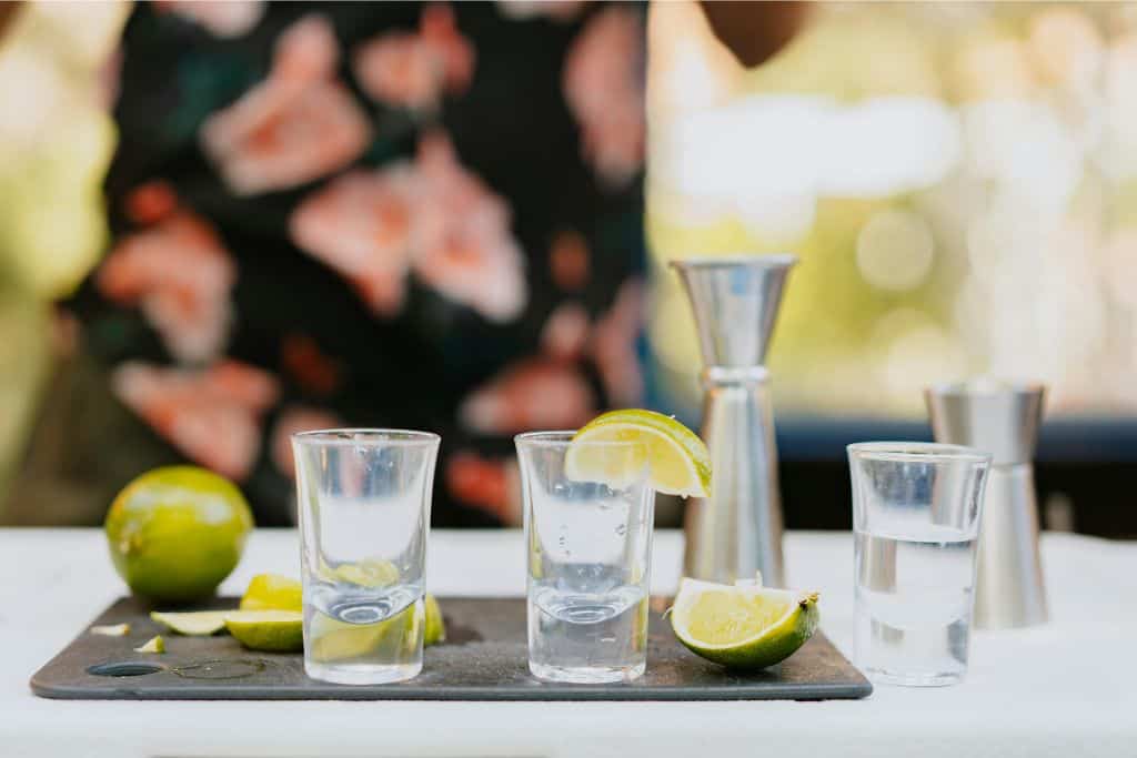 A table with a spirit measurer and shot glasses on it with lime and lemon slices.
