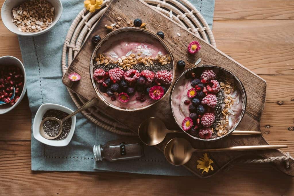 Two wooden bowls on a wooden try with smoothie in them using fruits including raspberries.