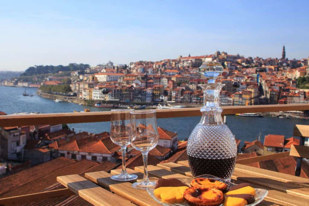 A carafe of red port sat next to two empty port galsses on a tray on a table outside.  The table is on the terrace of the Taylors cellar which is one of the best wineries in Porto Portugal.
