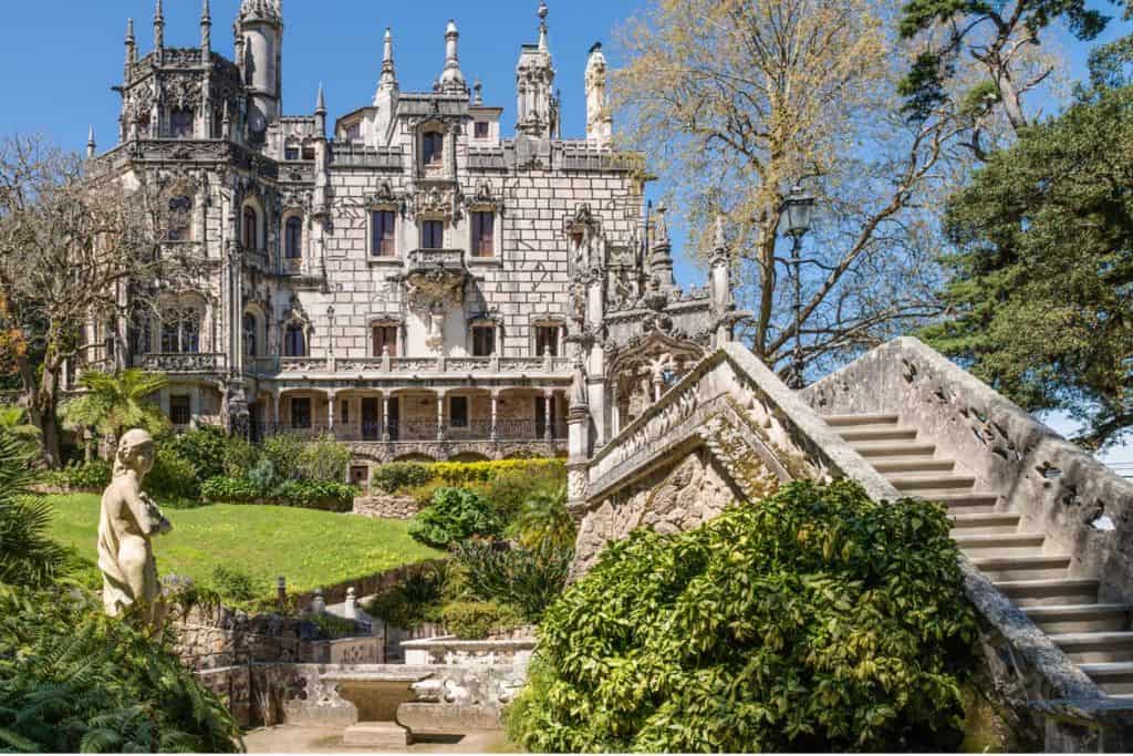 There is a large country house with towers and turrets. The facade of the house is made up of bricks. It is Quinta da Regaleira near Lisbon in Portual and is fun to visit with kids.