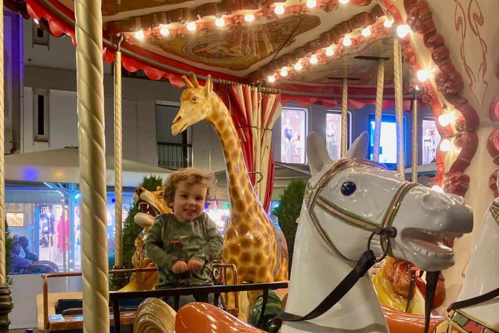 A toddler is sat on an animal-themed carousel in Lagos in Portugal.