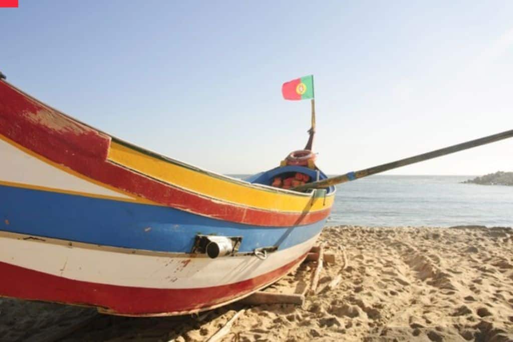 A Portuguese fishing boat on the beach.  It has stripes of yellow, blu and white paint around it.  