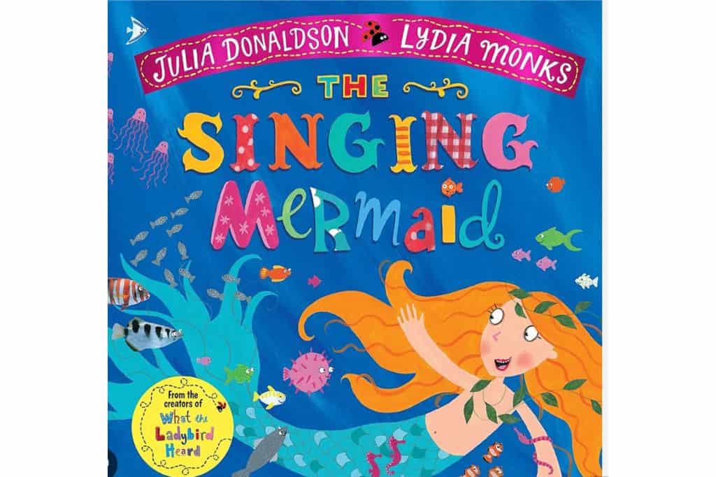 The front cover of The Singing Mermaid one of the best audiobooks for family road trips. The cartoon mermaid is surround by other sea animals.