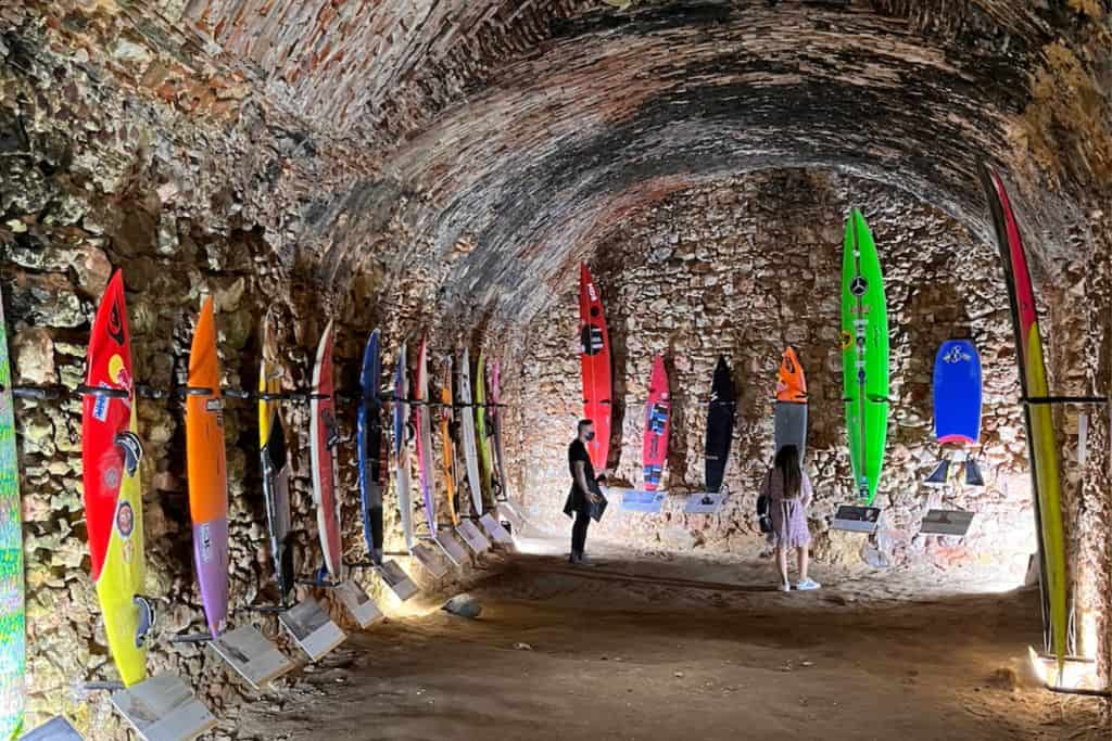 The inside an old brick fort with two people stood in front of a selection of surfboards. This is the surf museum in Nazare which is just a day trip to Lisbon.