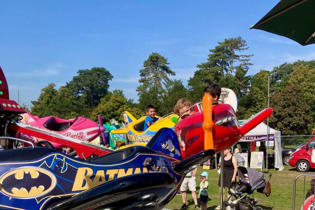 There is an airplane kids ride and the red airplane is coming towards the person taking the photo. In the airplane are two boys. This is at Big Eat Festival which is one of the best festivals in Hampshire.