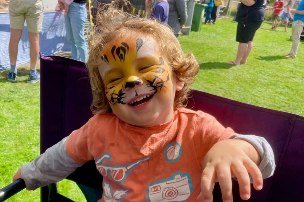 A little boy is laughing at the camera with tiger face paint on and is pretending to be a tiger.