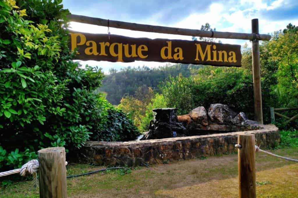 There is a path in the front of the image. There is also a wll and then in the air in the centre of the image is a sign that reads "Parque da Mina" which is in the Algrave.