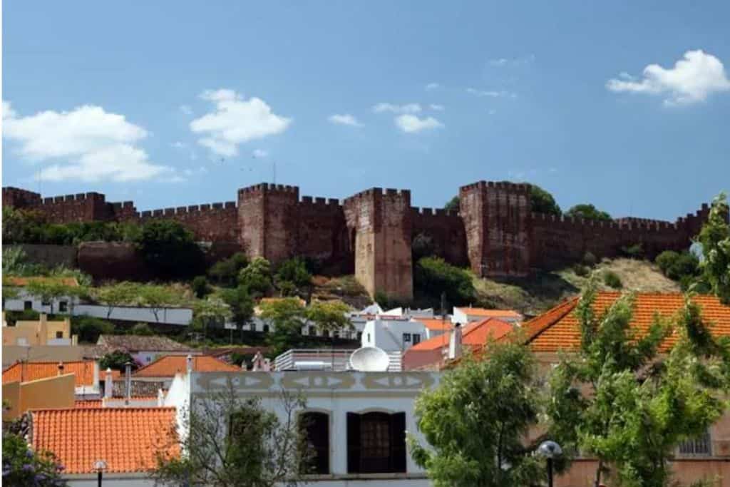 In the back of the image is Silves Castle in the Algarve with it's castle walls. In the front of the walls are some local homes and buildings. 