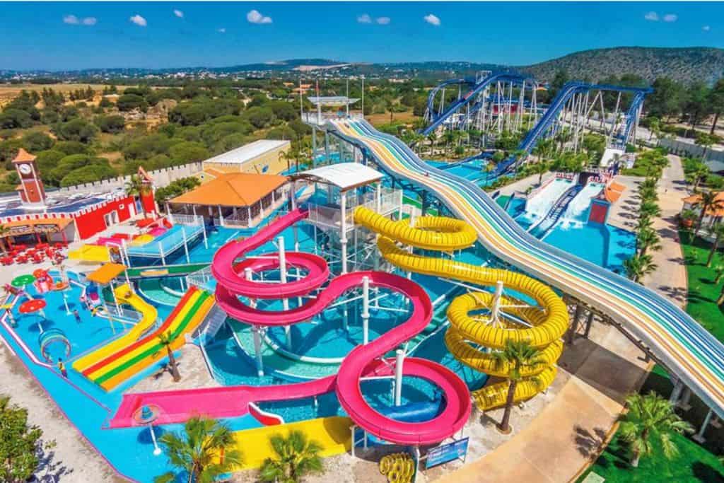 This is a water park and there are lots of brightly coloured slides going into a large swimming pool taken from above. Behind it are lots more slide as well.  This is Aquashow waterpark which is one of the best things to do with kids in the Algarve.