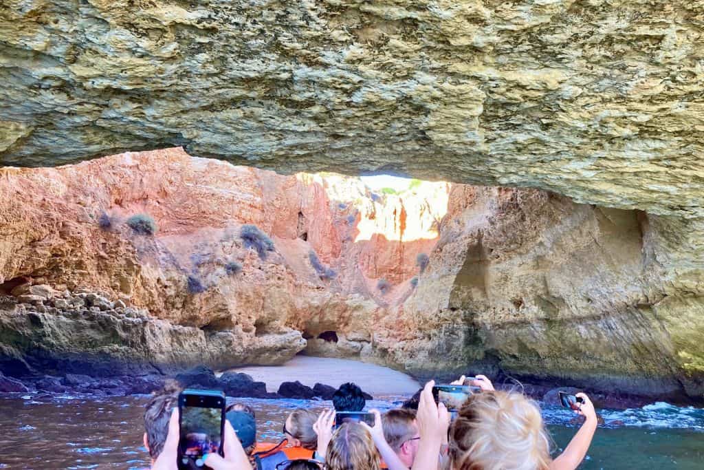 The image is taken from. boat tour in the Algarve.  In the bottom of the image are the backs of peoples heads in the front row of the boat.  In front of them is the entrance to the Benagil Cave which is one of the best things to do with kids. 