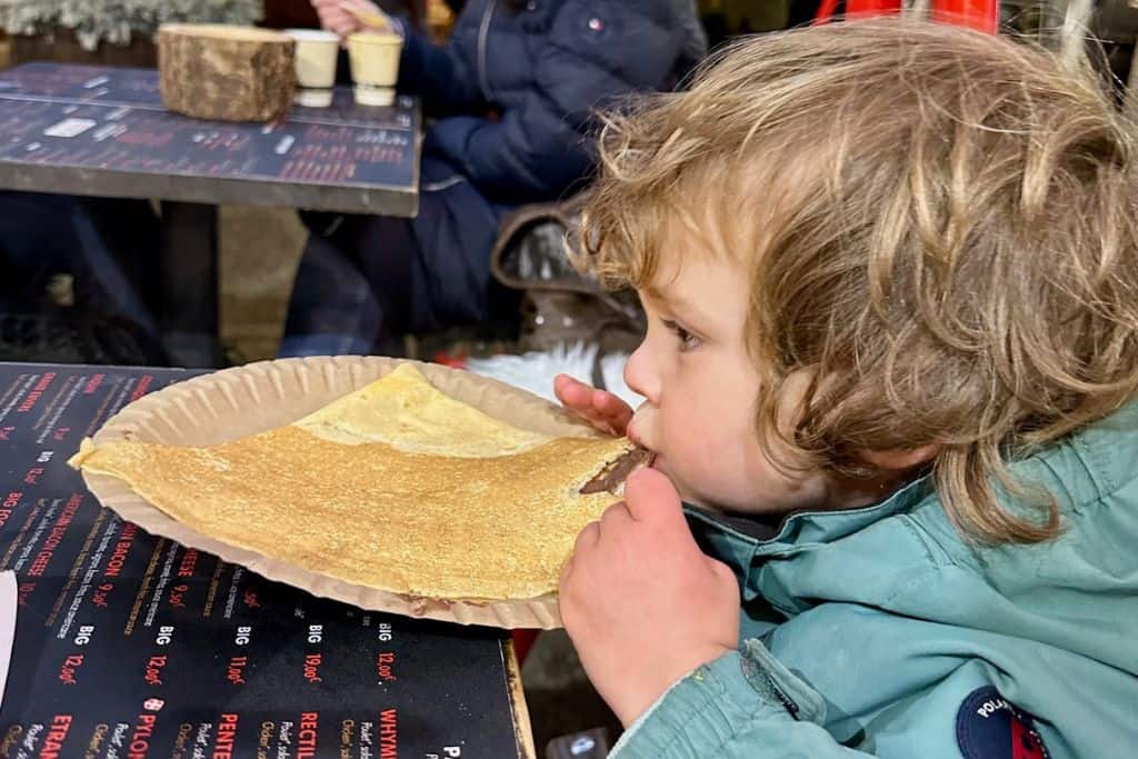 A close up of the side profile of a young boy eating a chocolate crepe.