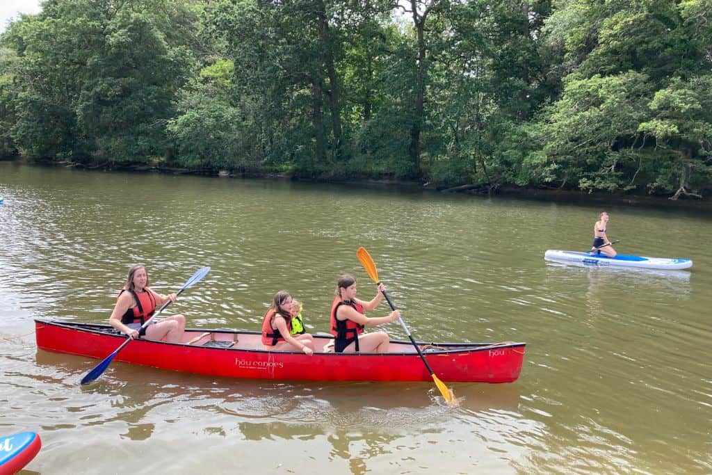 A woman is in a  red canoe with two girls and a little boy. They are on the River Hamble and having fun paddling for the afternoon.