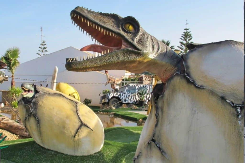 This is a minigolf course in the Algarve. In the right of the image is a huge egg and a dinosaur is coming out of it.  Opposite on the left is a smaller egg which is cracked with a smaller dinosaur coming out of it. 