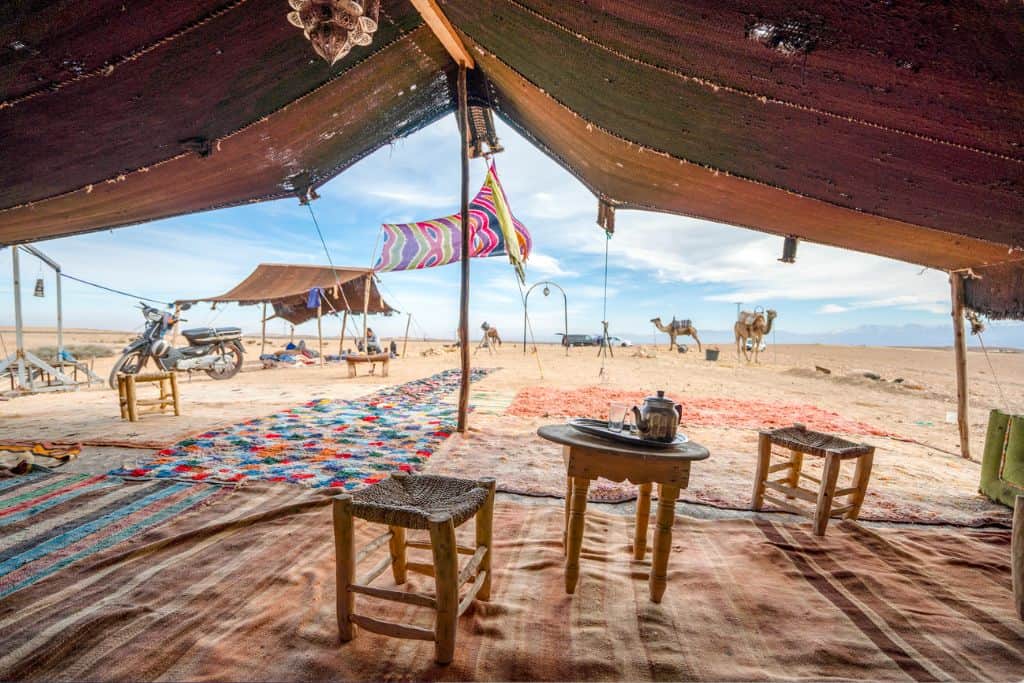 The Agafay Desert in Marrakech being viewed as though the person taking the photo is sat in the tent;  There is a small table and chairs set-up for drinking some Moroccan tea.