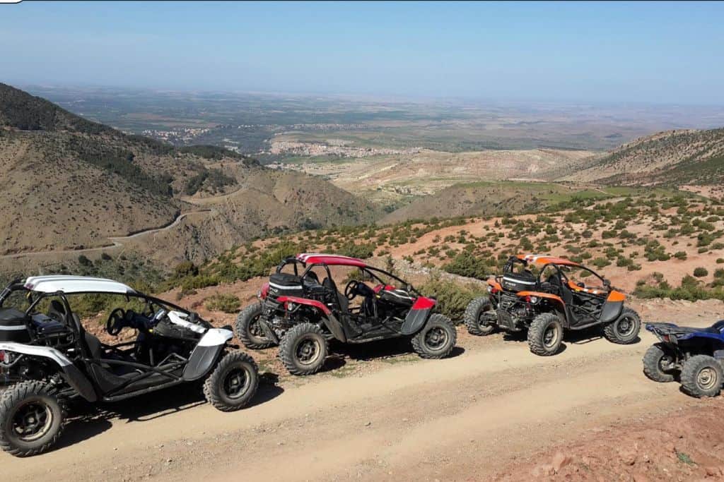 Three dune buggies are facing the the right. The first is green, the middle one red and the last one black. In the background is Marrakech. This is something that you can do with kids.