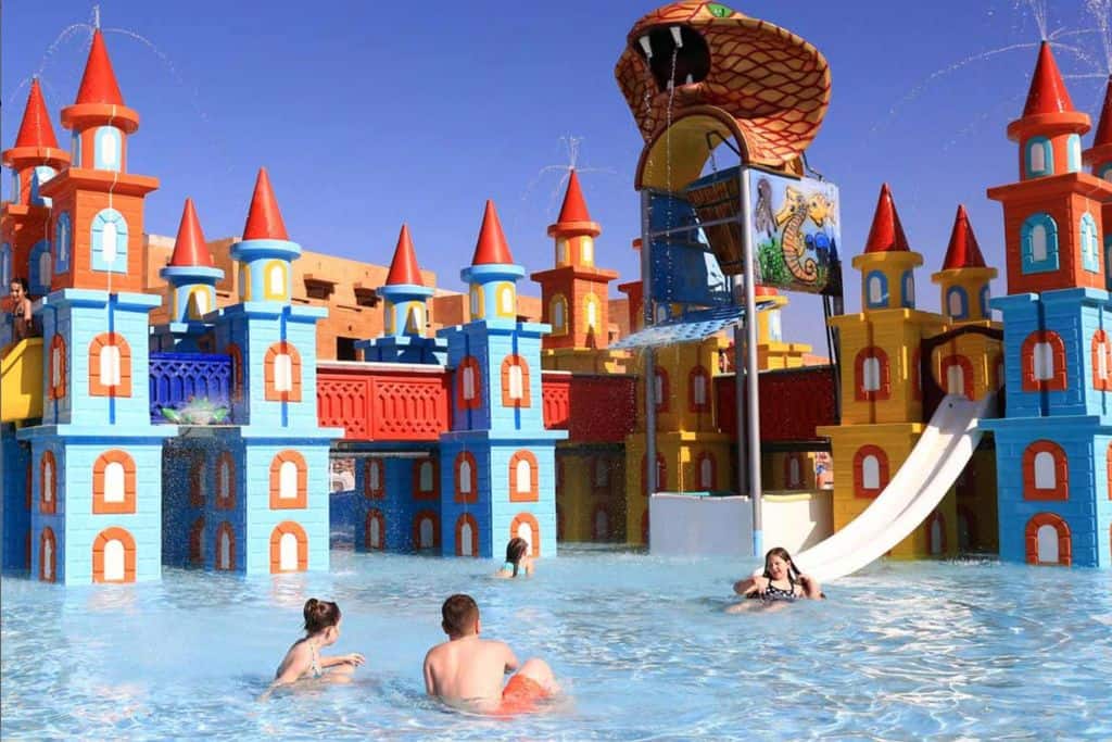 This is the image of a waterpark in Marrakech with kids on the slide. The slide is part of a castle set-up. In the front is a family with their backs to the person taking the photo.
