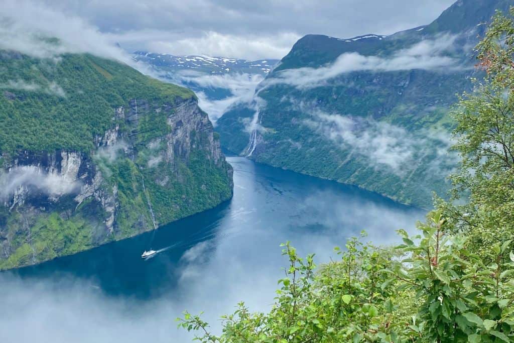 View from up high of the Geirangerfjord.  There is the water running through the fjord.  And on the fjord walls are the lush green plants.  The view is taken from Eagle Road.