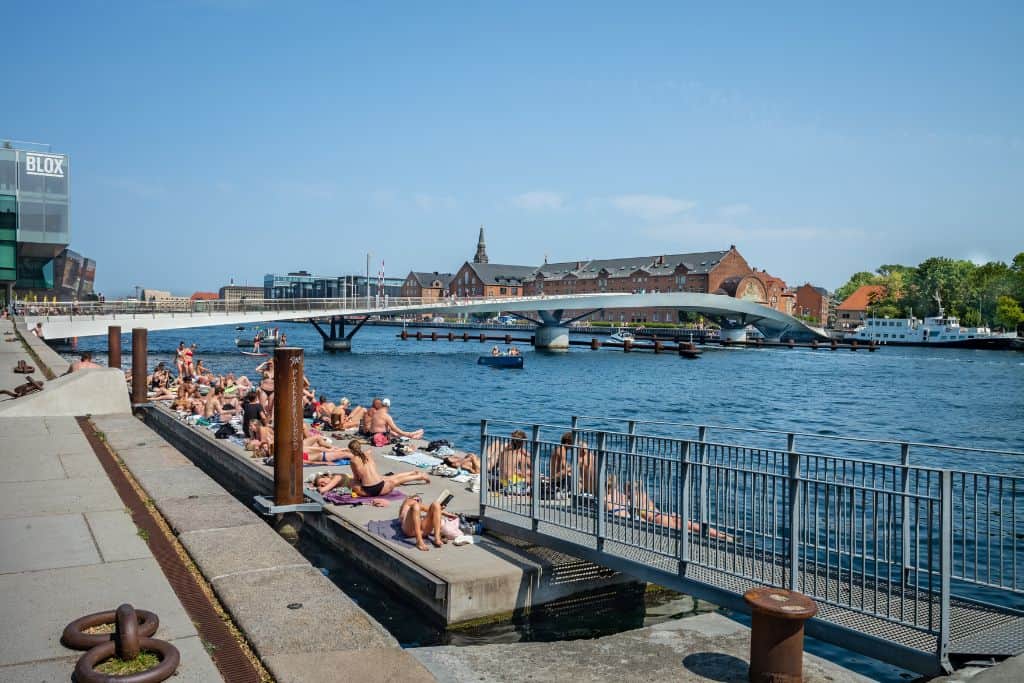 This is a photo of the harbour in Copenhagen with people lying on the waterfront enjoying the sunshine.  This is in Copenhagen.