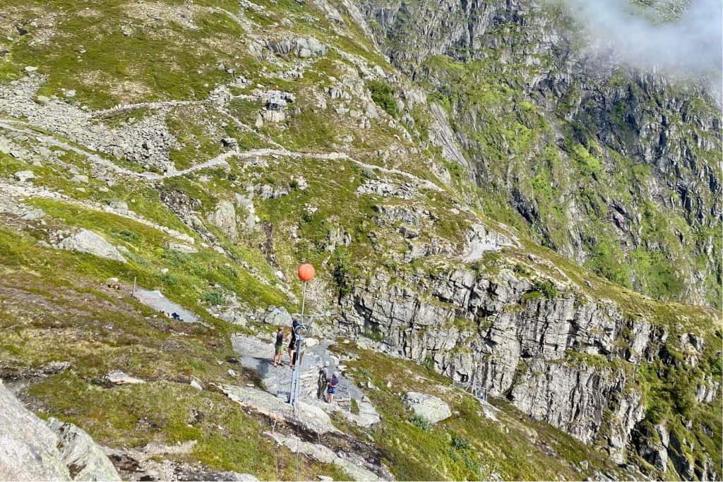 This is a view of the side of a mountain with green grass.  On the mountain are some people who are riding the Loen Zipline in Norway.