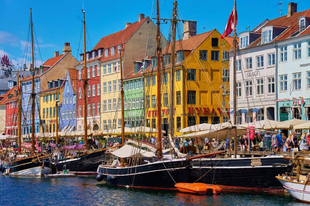 The view of Nyhavn in Copenhagen from the water looking at the colourful waterfront buildings.  In front of the buildings are several sailing yachts.