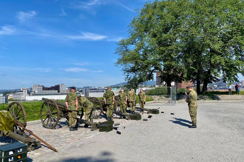 The Aker Fortress in Oslo  with some army soldiers preparing the cannons for firing. The view in front of them is over Oslo.