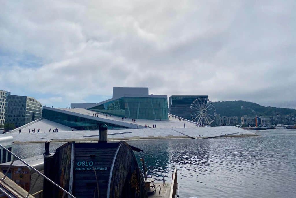 A view from the waterfront over to the Oslo Opera House.  In the front of the photo is a sauna building on the waterfront. 