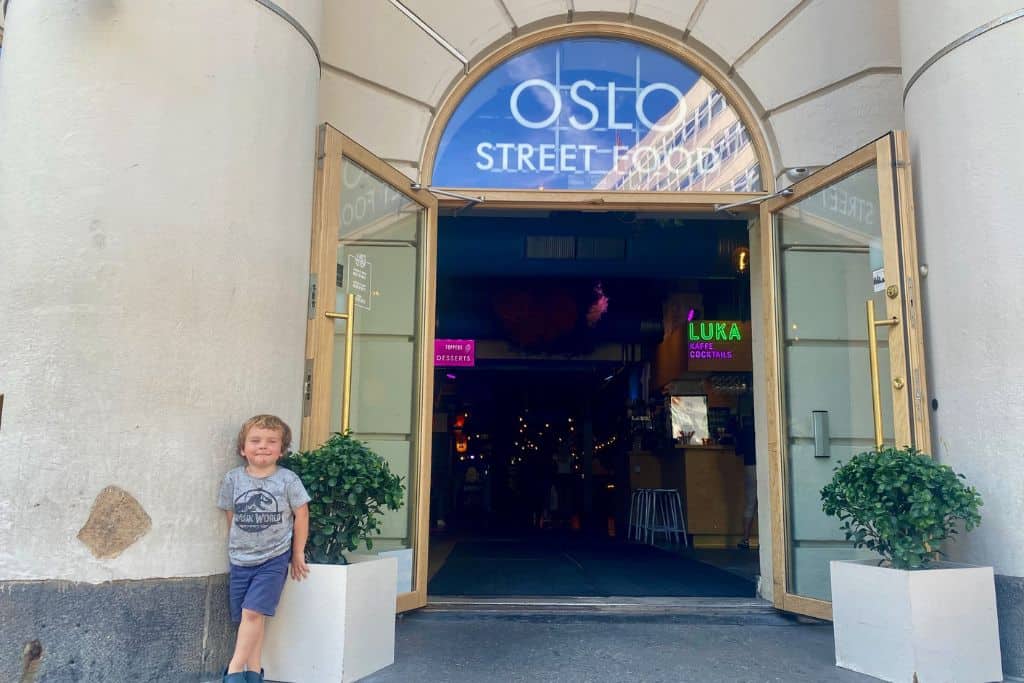 The outside of the Oslo Street Food building with a very young boy in a grey t-shirt stood next to the entrance door.  Heading their for street food is one of the best ways to end a day in Oslo. 