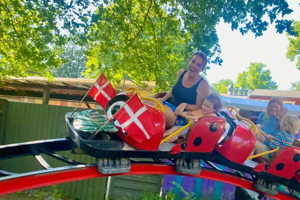 A woman and her young son are sat on a roller coaster in a theme park laughing as it goes around. They are both very happy and having a lot of fun with each other.  This is at Bakken which is a theme park in Copenhagen and perfect for visiting with kids of all ages.