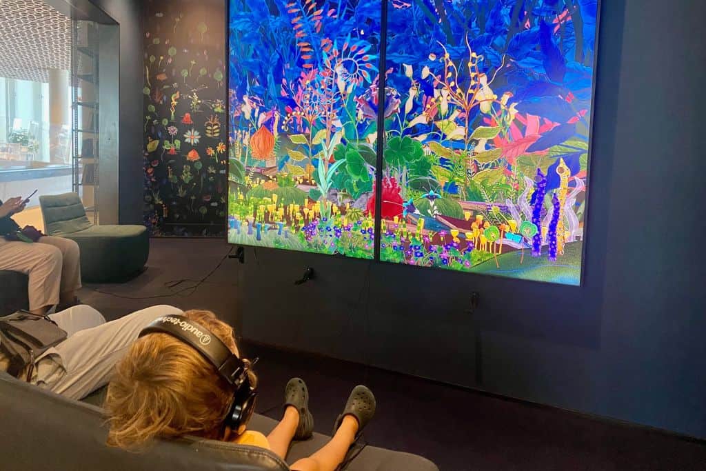 A little boy has his back to the camera and is sat on a sofa with some headphones on.  In front of him is an art installation involving plants that he is intently watching.   Oslo Library is a great place to head with kids if they need some indoor activities to try.