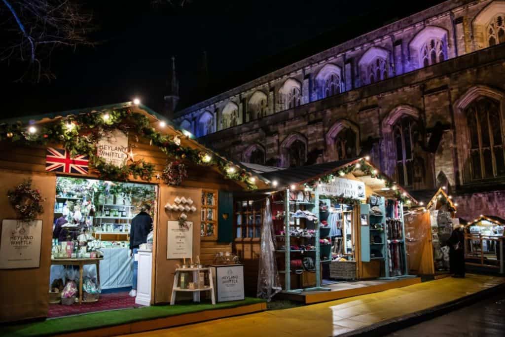 A row of wooden chalets set up for a Christmas market and behind them is Winchester Cathedral.